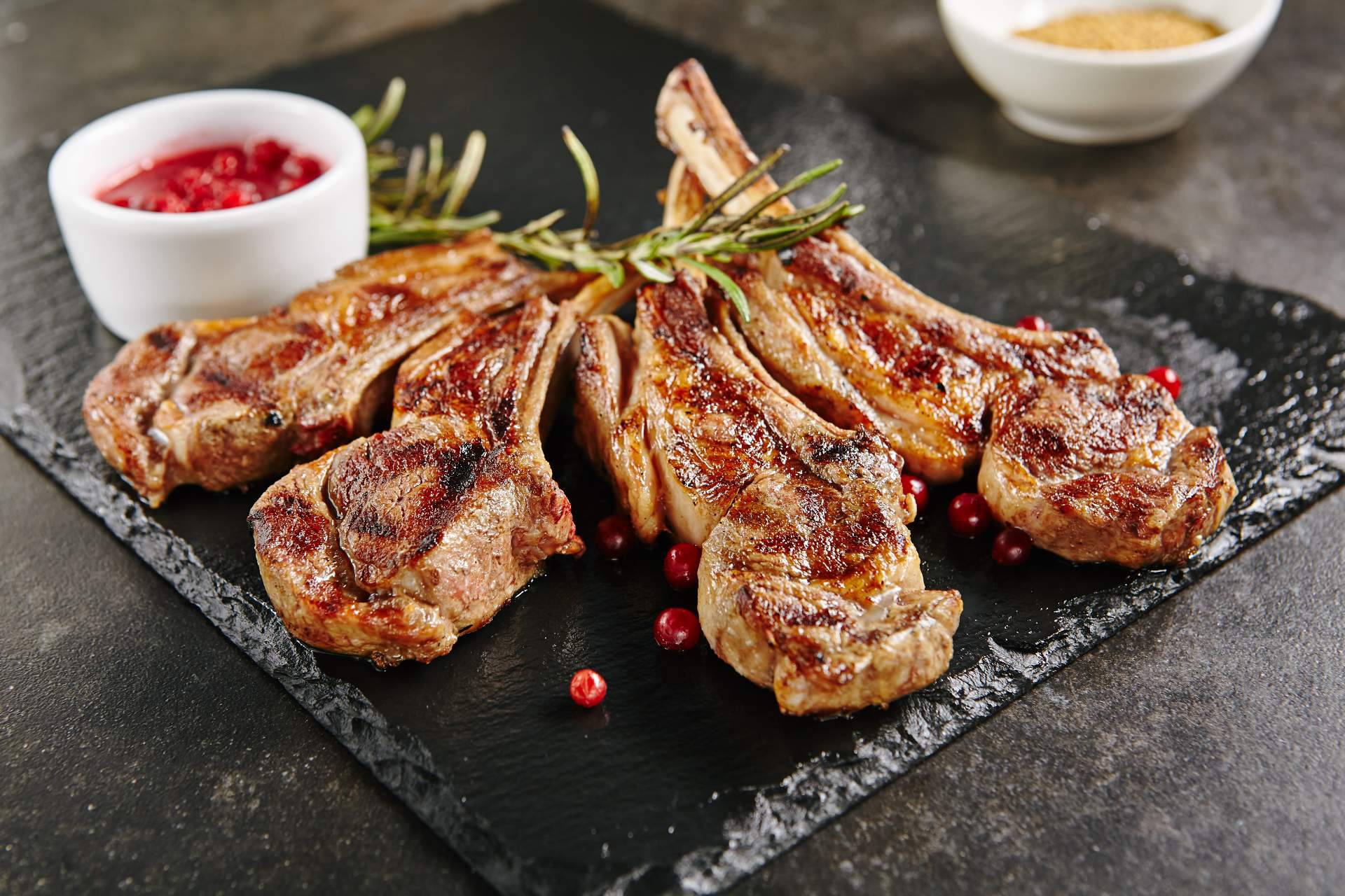 A slate plate with a selection of roast lamb chops and a pot of sauce