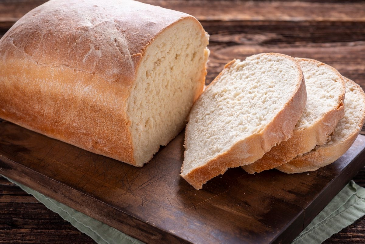 A tin loaf of fresh white bread with a few slices