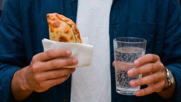 A man holding an empanada and a glass of water.
