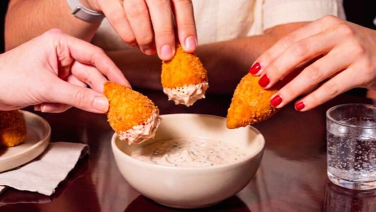 People dipping coxinhas in a condiment.