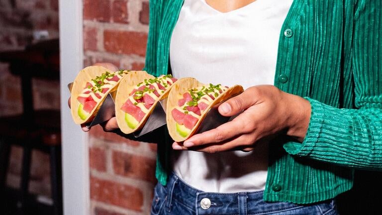 A person holding three tuna tacos.