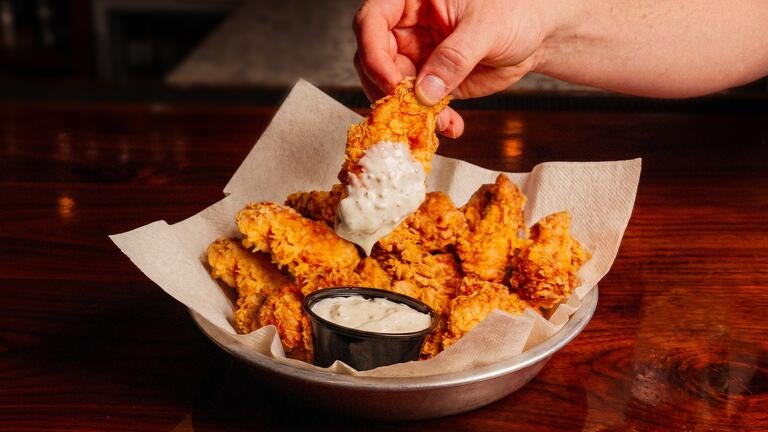 Breaded chicken wings being dipped into Buffalo sauce.