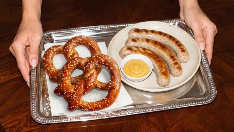 Pretzels and sausages and mustard on a silver platter.