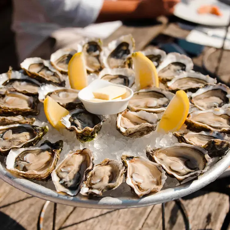 A platter of oysters with lemon wedges.