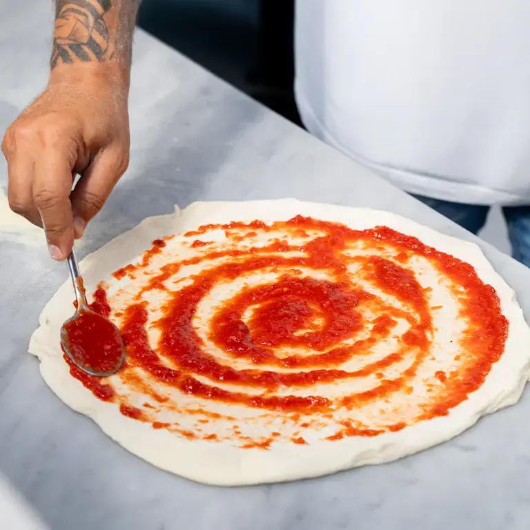 Tomato sauce being spread on pizza dough.