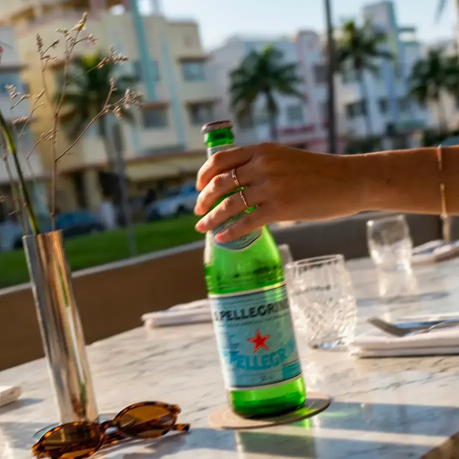 Hand holding a bottle of S.Pellegrino on a Miami restaurant terrace.