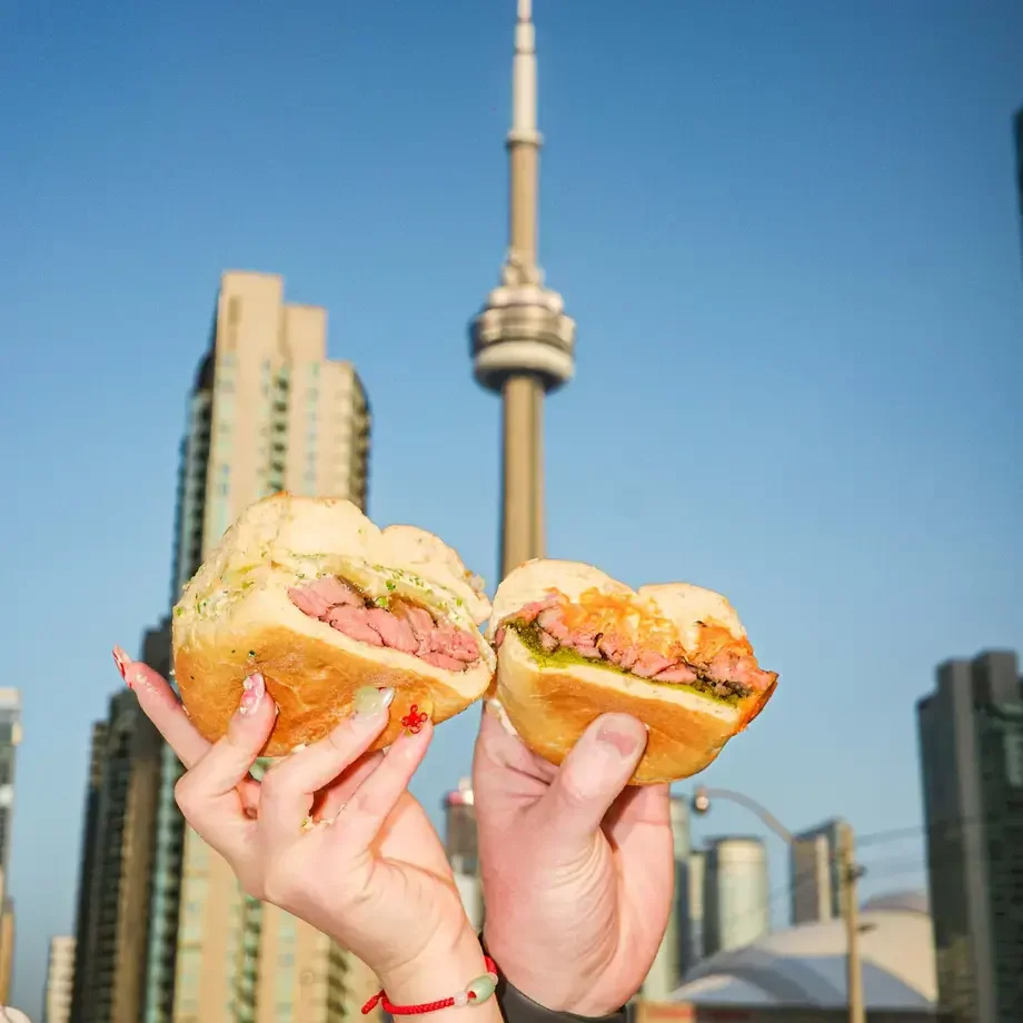 People holding sandwiches with Toronto's CN Tower in the background.