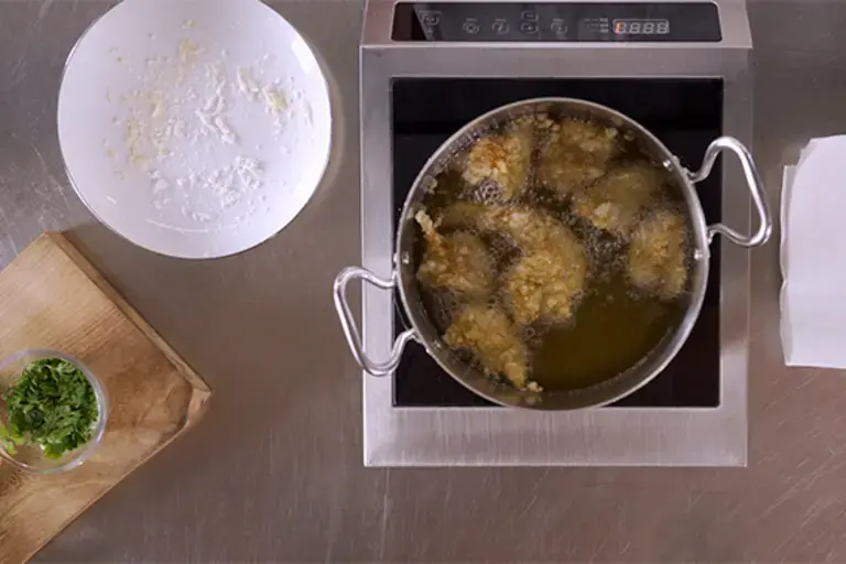 Chicken being fried in a pot of oil.