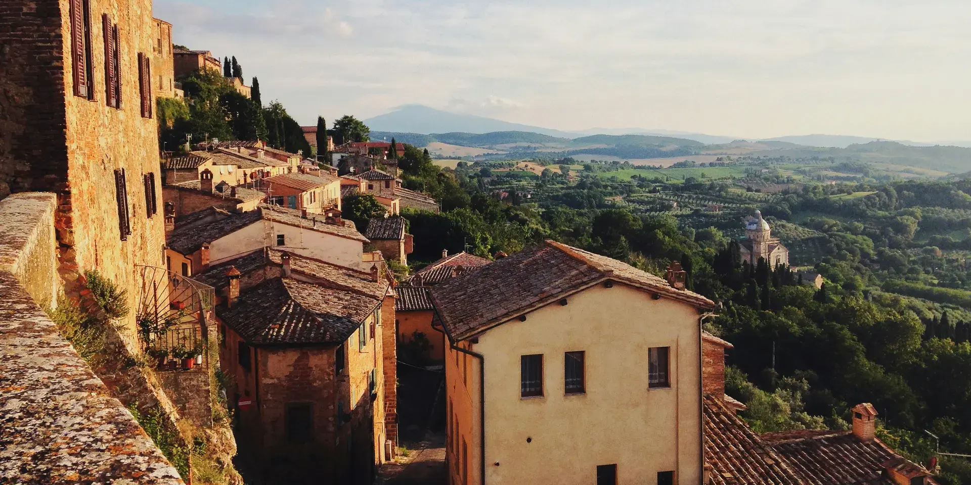 Sunlit Tuscan village with rustic terracotta rooftops, rolling green hills, and a scenic view of a distant church