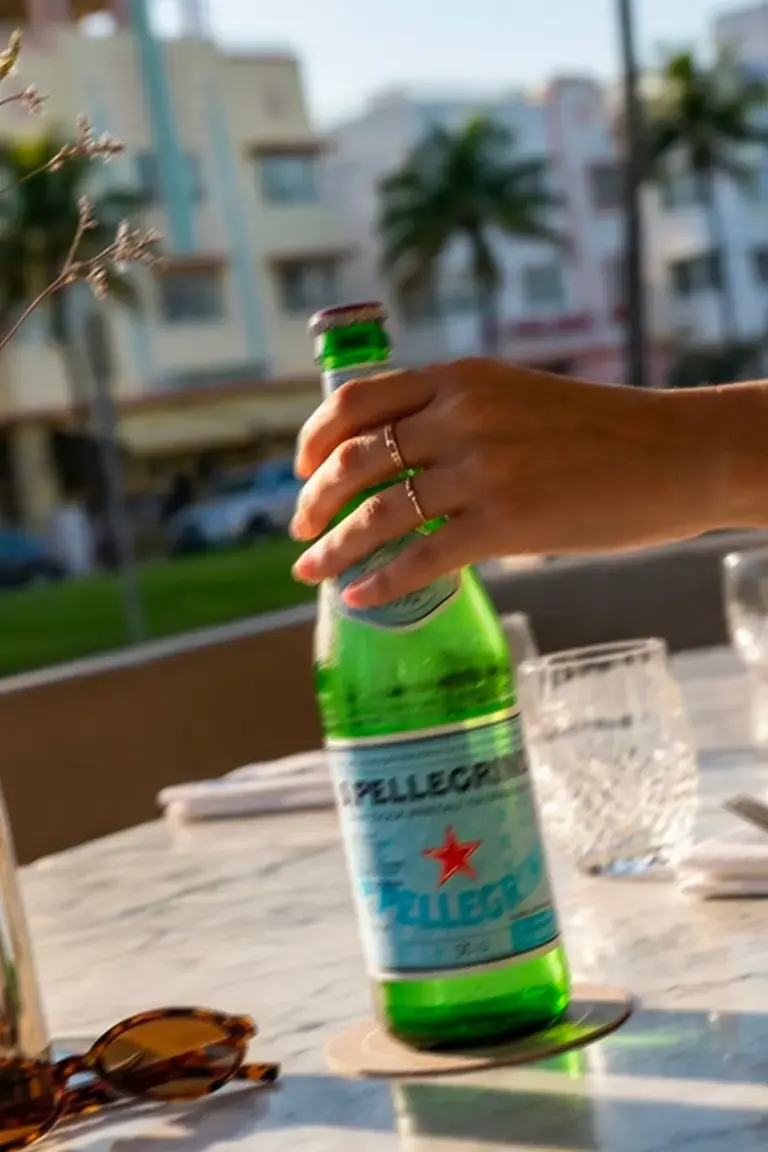 Hand holding a bottle of S.Pellegrino on a Miami restaurant terrace.