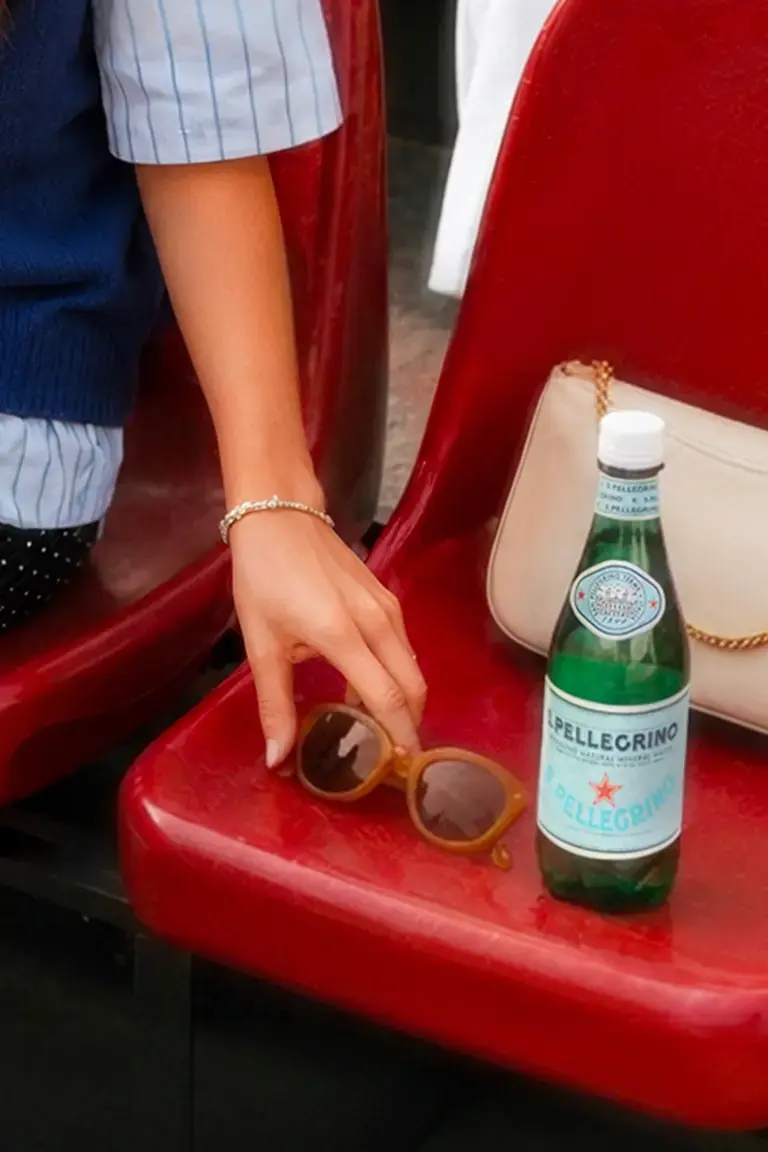 A person with a bottle of S.Pellegrino on a red seat.