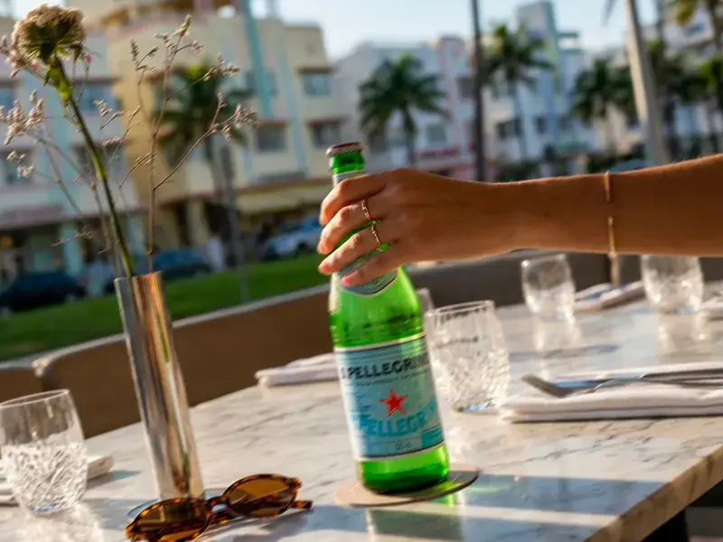 Hand holding a bottle of S.Pellegrino on a Miami restaurant terrace.