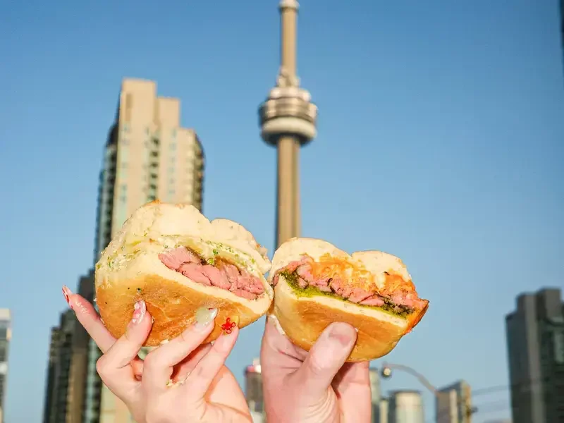 People holding sandwiches with Toronto's CN Tower in the background.
