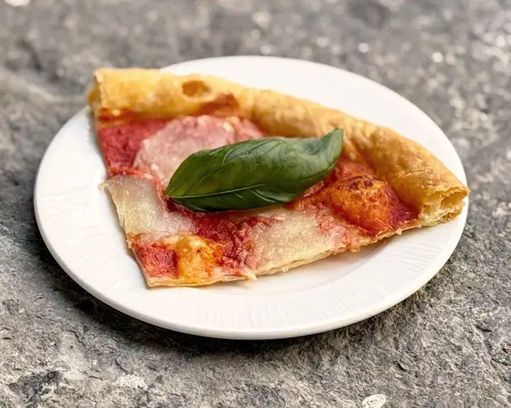 Slice of puff pastry pizza with tomato and pesto.