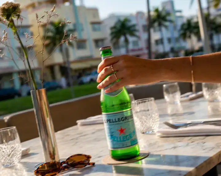 Hand holding a bottle of S.Pellegrino on a Miami restaurant terrace.