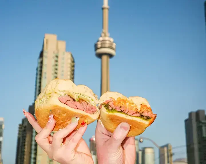 People holding sandwiches with Toronto's CN Tower in the background.